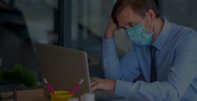Homem preocupado em frente ao computador, trabalhando em escritório usando máscara cirúrgica