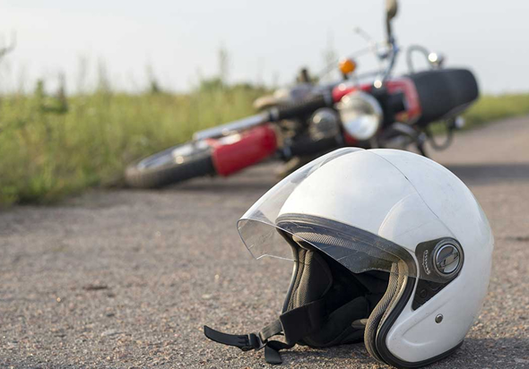 Capacete de motociclista caído no chão, atrás moto tombada para o lado