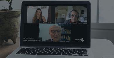 Laptop sobre uma mesa, na tela aparecem as imagens de uma mulher e dois homens, todos conversando em uma videoconferência.